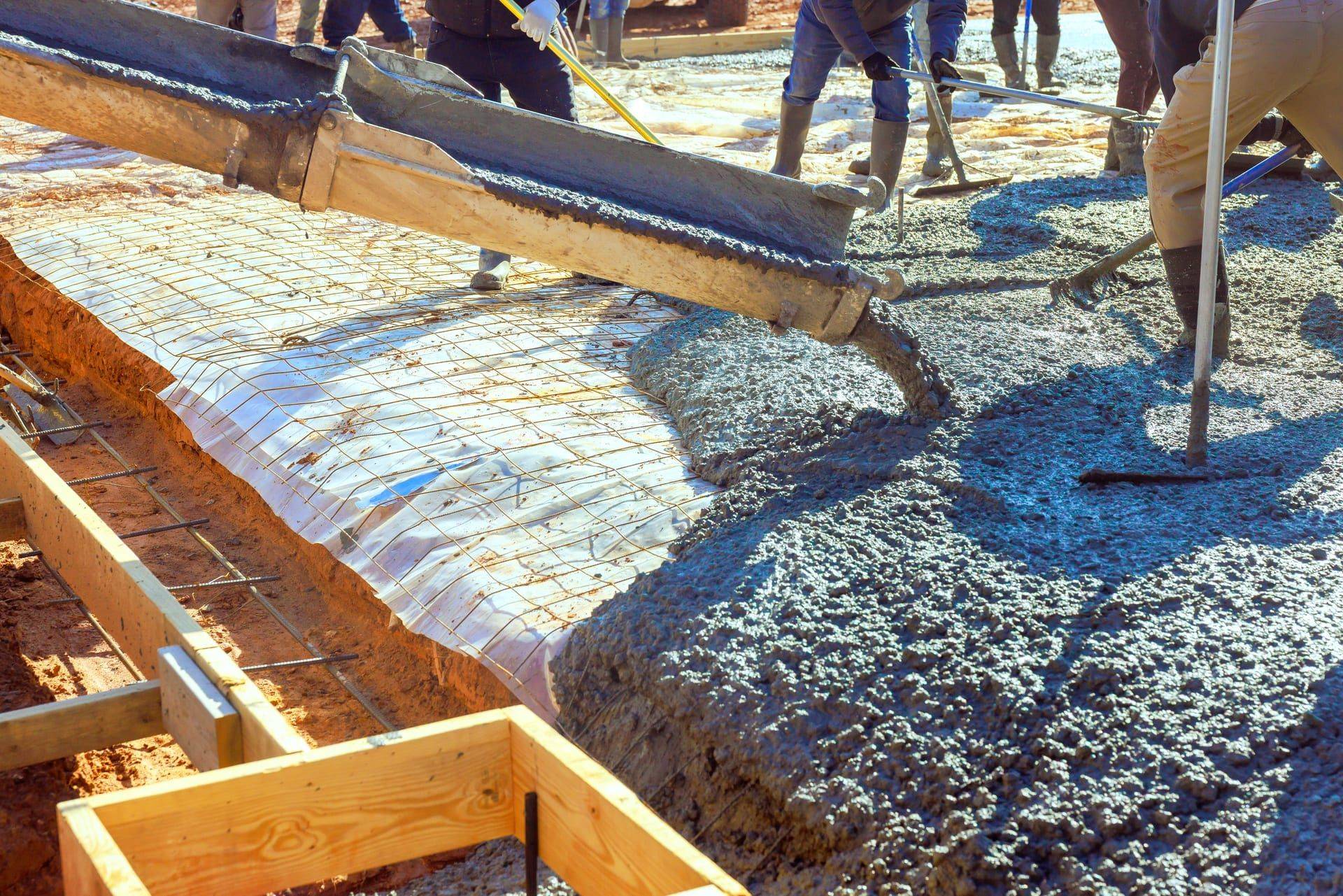 Construction workers pouring wet concrete into a rebar-reinforced foundation form on a Bay Area job site